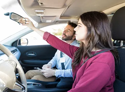 Femme ajustant le rétroviseur intérieur d'une voiture, moniteur de conduite à côté à Toulouse en Haute-Garonne 31