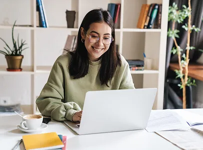 Jeune femme souriante travaillant sur un ordinateur portable, avec café et livres à Toulouse en Haute-Garonne 31